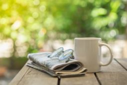 Zeitung, Brille und Kaffeetasse auf Holztisch vor grünem Hintergrund